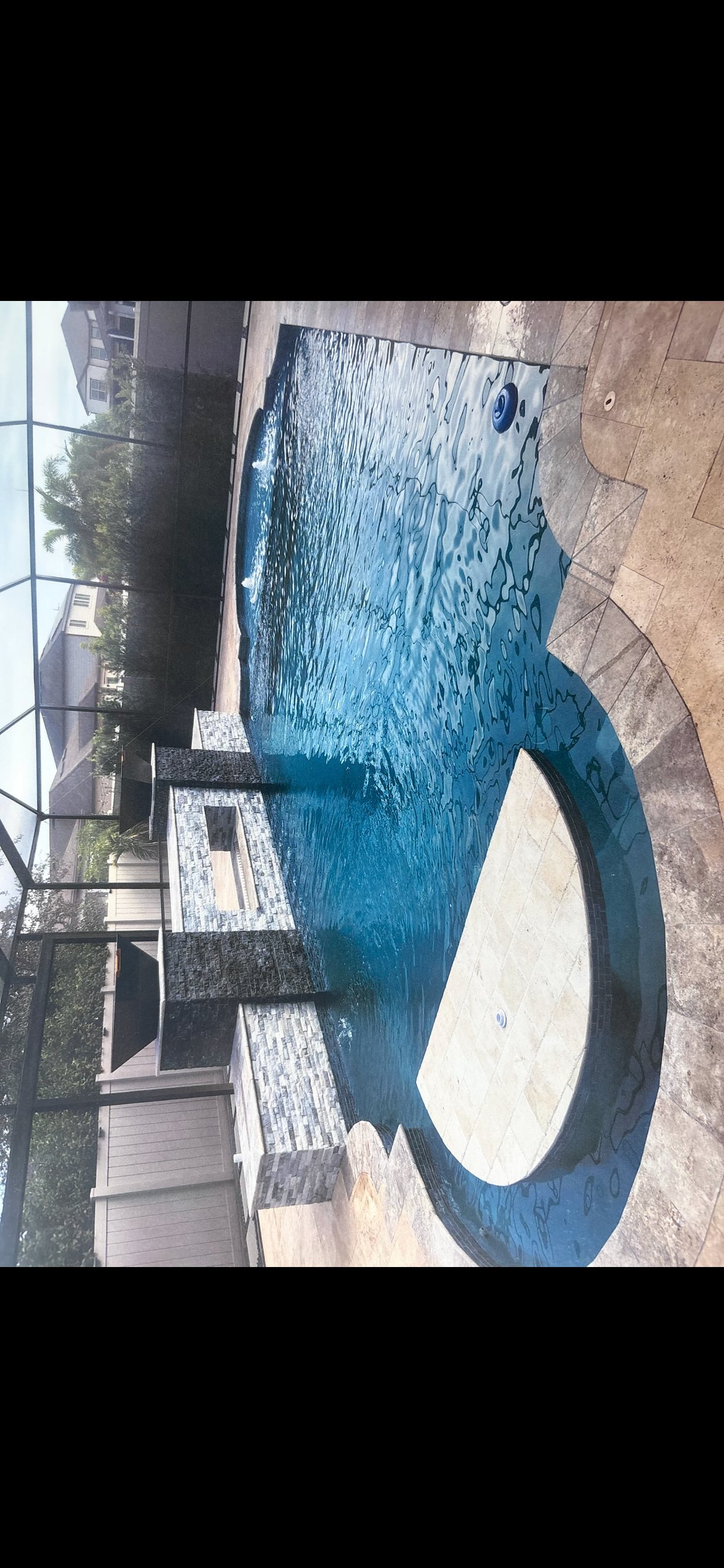 Overhead view of a residential swimming pool with blue water and white interior, surrounded by concrete patio and adjacent buildings