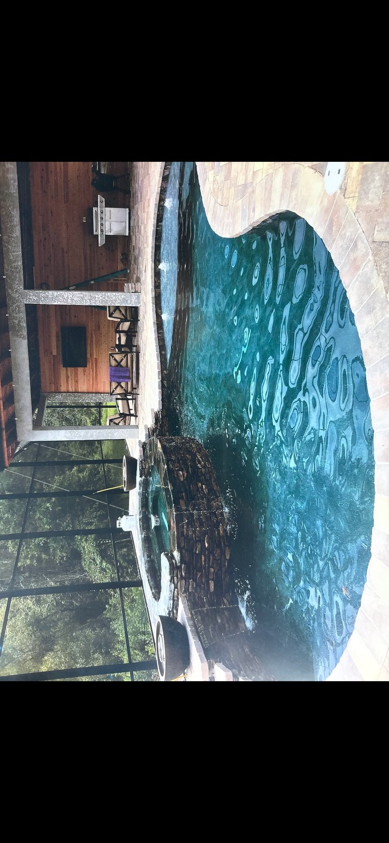 Brick house with brown wooden door next to green water with tire pattern, viewed from rotated angle